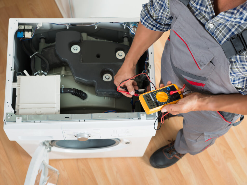 High angle view of technician checking washing machine with digital multimeter in kitchen